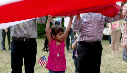 Imagen de una niña inmigrante ayudando a desplegar una bandera