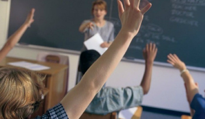 Imagen de una clase con niños levantando la mano