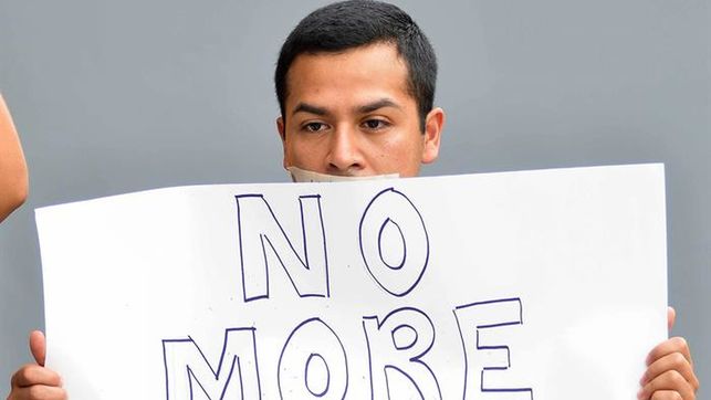imagen de un joven hispano con la boca tapada con cinta y una pancarta (no más)