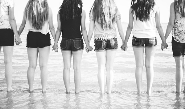 un grupo de mujeres blancas de espaldas cogidas de la mano en la orilla del mar