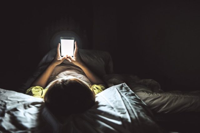 un niño acostado en una cama mira un smartphone