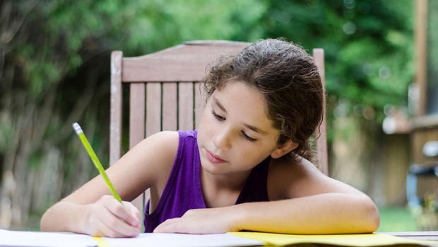 una niña escribe en una mesa al aire libre